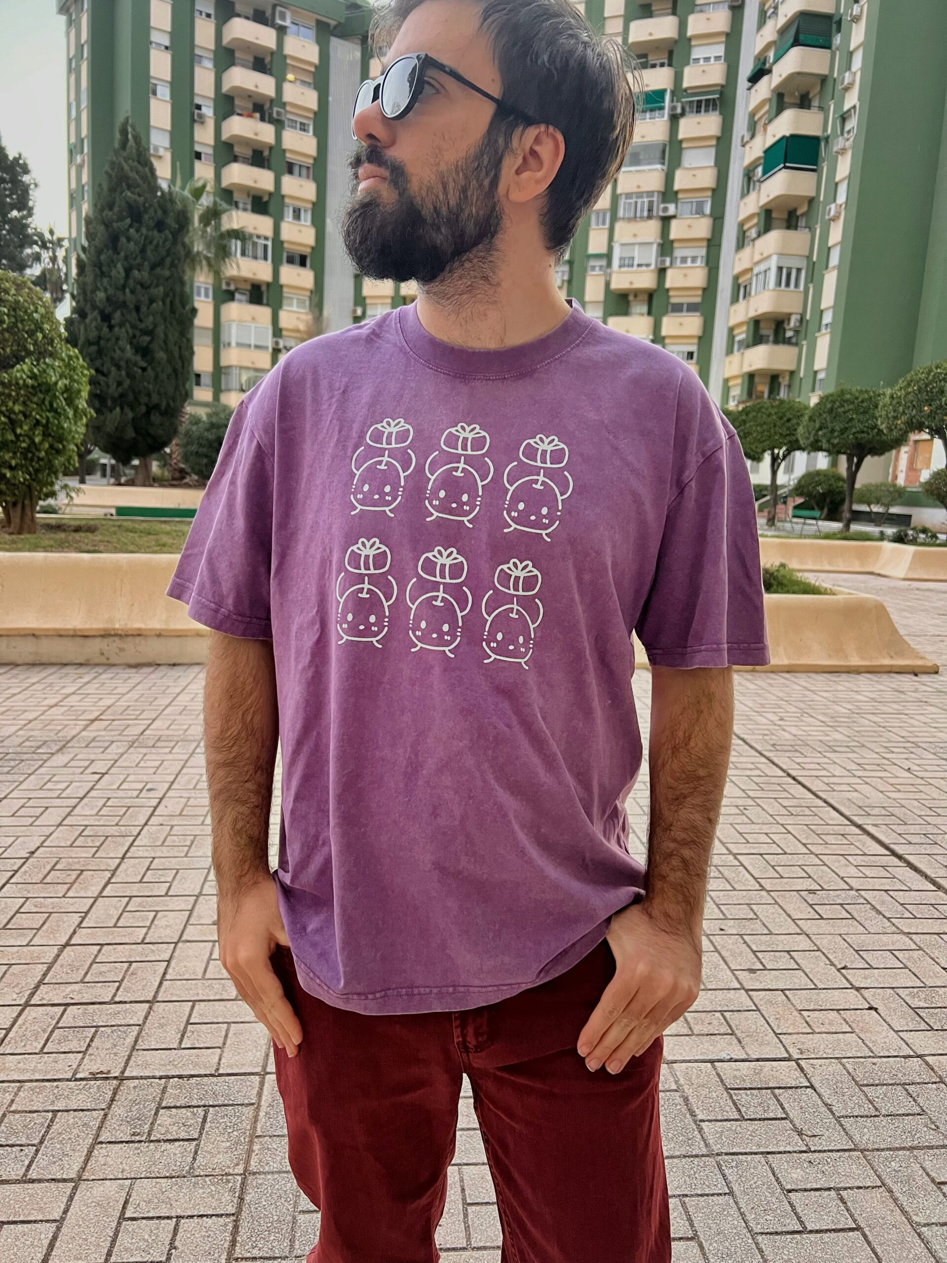 Camisetas de junimos sosteniendo regalos. Diseño en blanco. Los colores de la camiseta pueden ser en negro o en morado. Los modelos son una mujer con la camiseta negra y un hombre con la camiseta morada