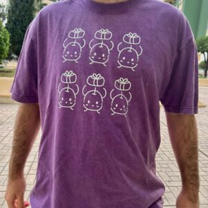 Camisetas de junimos sosteniendo regalos. Diseño en blanco. Los colores de la camiseta pueden ser en negro o en morado. Los modelos son una mujer con la camiseta negra y un hombre con la camiseta morada