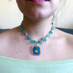 Collar stardew valley artesanal con una semilla de carambola en el centro como charm acrílico. El resto de cuentas son de vidrio azul y tiene pequeñas gotas azules que cuelgan