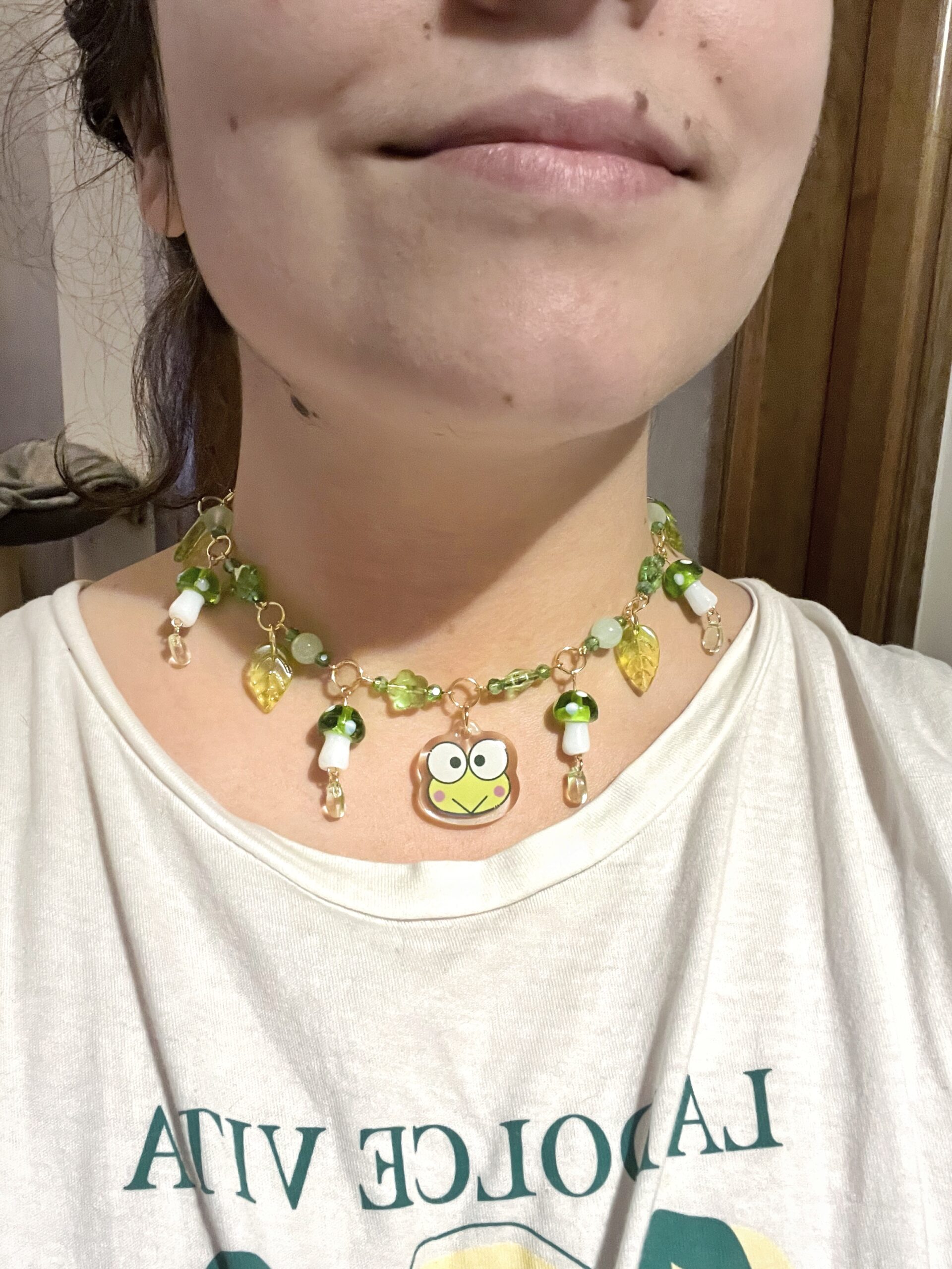 Collar Sanrio con un Keroppi (rana verde) en el centro. Metal de acero inoxidable con baño de oro del que cuelgan abalorios y setas verdes