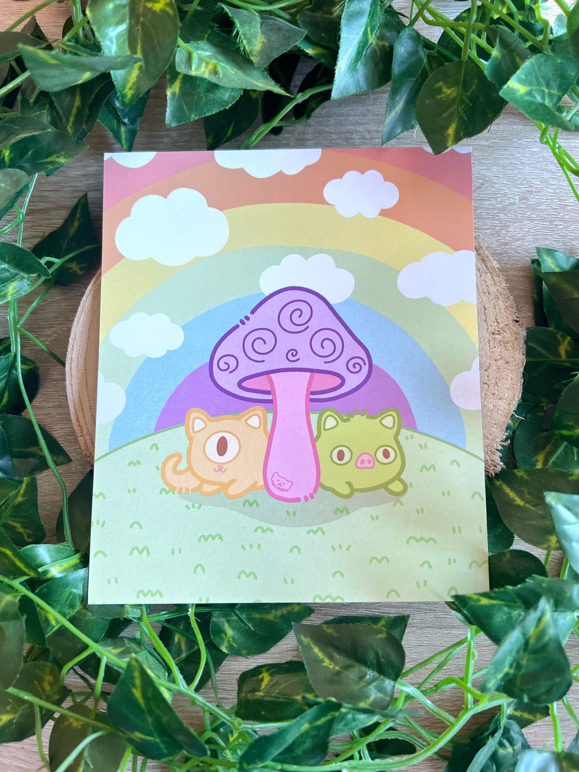 Ilustración de Oniria, un juego de rol narrativo surrealista que presenta a Muk, un gato verde camaleón con nariz de cerdo y a Chester, un gato serpiente naranja y cíclope, escondidos tras una seta- Están sobre césped y el fondo es un arcoíris saturado con nubes